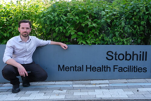 Adam Harley bending down next to the Stobhill Mental Health Facilities sign. 