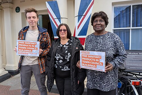 Cllr Nathan Hunt, Cllr Jo Harvey, and Cllr Padrica Pennington holding signs that read "Free Sanitary Products in Town Council Buildings"