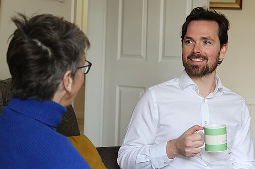 Adam Harley sitting down with a mug talking with a resident.