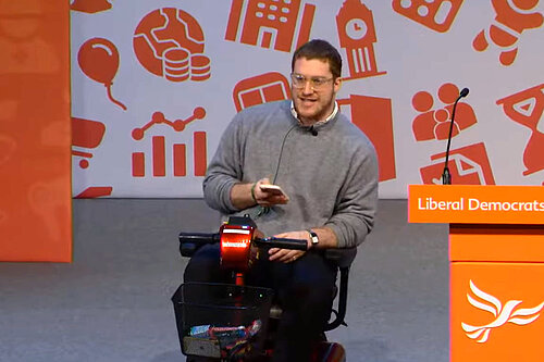 Jonah Weisz in wheelchair at Party Conference speaker podium