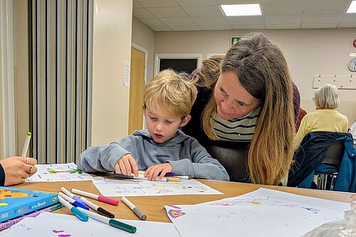 Vikki stood over a child doing some colouring in at a table