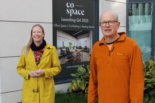 Councillors Helen Campbell and Paul de Kort are standing in the Jubilee Square development, in front of a posted announcing the launch of Co-Space St Albans.