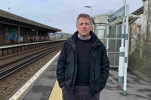 James MacCleary standing on the platform at Newhaven Harbour station. Behind him are empty tracks, station buildings and signalling paraphrenalia