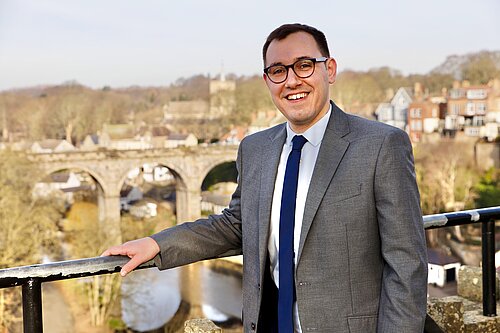 Tom standing in front of a backdrop of Knaresborough